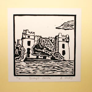 Peut inclure: Gravure sur linoléum en noir et blanc d'un château avec un arbre devant. L'estampe est intitulée "Bishop's Castle" et signée "E. Duffy".