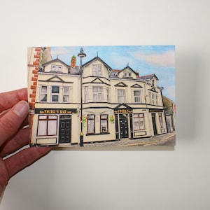 Könnte beinhalten: Eine handgezeichnete Illustration eines Pubs namens "Friel's Bar" mit einer gelben Fassade und schwarzen Verzierungen. Der Pub hat ein Schild über dem Eingang, auf dem "Friel's Bar" steht.