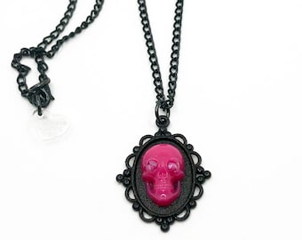 May include: A black chain necklace with a pink skull pendant in a black ornate frame.