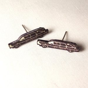 May include: A pair of black and white wooden earrings shaped like a vintage car. The earrings are on a white surface.