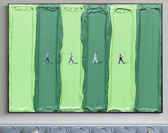 May include: Abstract artwork with vertical green stripes and tiny figures of people walking across. The painting is framed and displayed above a blue sofa with floral cushions. The artwork uses shades of green.