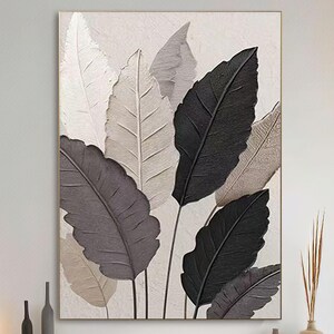 May include: A large canvas artwork depicting textured leaves in white, grey, and black. The leaves are arranged vertically against a neutral background, creating a modern, minimalist aesthetic. The artwork is framed, suitable for interior decor.