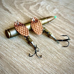 May include: Two copper fishing lures with black hooks and a silver bullet casing. The lures have a textured, diamond-shaped pattern.