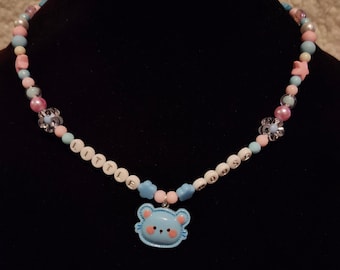 Puede incluir: Un collar de cuentas azul pastel con un dije de oso azul y cuentas de letras blancas que deletrean "LITTLE MOUSE".