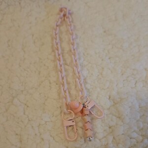Op de afbeelding: Een roze plastic ketting met twee roze clips en een roze kralenbedel. De ketting is gemaakt van in elkaar grijpende schakels en de bedel is een reeks stervormige kralen.