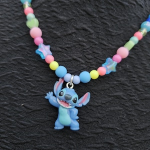 Op de afbeelding: Een kleurrijke kralenketting met een blauwe Stitch-hanger. De ketting heeft een verscheidenheid aan kralen in pastelkleuren, waaronder roze, blauw, geel en groen, met stervormige accenten. De hanger is een stripfiguur.