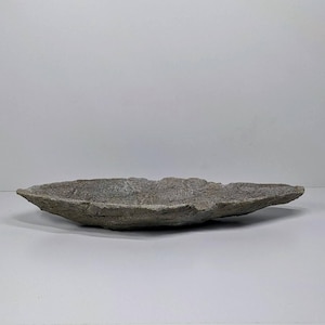 May include: A gray, oblong-shaped stone bowl with a rough, textured surface. The bowl has a shallow depth and is ideal for decorative purposes. The bowl is approximately 12 inches long.