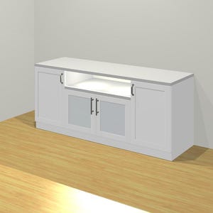 May include: A white cabinet with a rectangular top and a recessed open shelf. The cabinet has two doors on each side and two glass-paneled doors in the center. Black handles and hinges are visible. The cabinet is set against a white wall and a wooden floor.