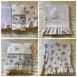 May include: A collection of folded fabric items including a solid light pink piece, a cream piece with floral fan patterns and lace trim, and a striped piece with floral accents and lace trim, all featuring ruffled edges and soft pastel tones.
