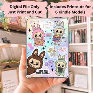 以下が含まれることがあります： 本とKindleを持っている、コスチュームを着た漫画のウサギが描かれた、カラフルなステッカーが付いた透明なケース。「Bookish」、「In my bookish era」、「I know what you're reading」などのテキストがステッカーに書かれています。画像には「Digital File Only Just Print and Cut」と「Includes Printouts for 6 Kindle Models」というテキストも含まれています。