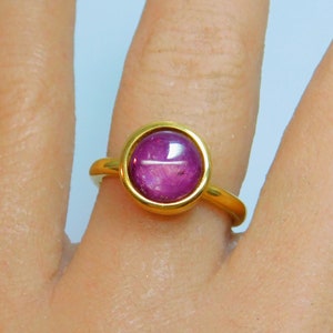 May include: A gold ring with a round, cabochon-cut, purple gemstone.