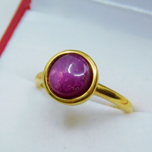 May include: A gold ring featuring a round, cabochon-cut ruby gemstone. The ruby is a deep pink colour and has a star-like pattern.