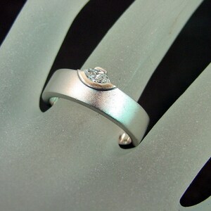 May include: A silver ring with a single, clear diamond set in a curved, prong setting.