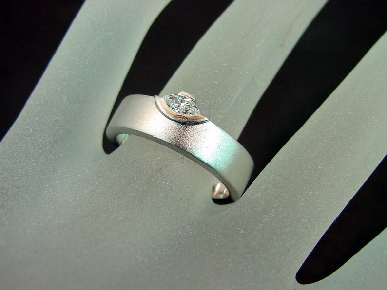 May include: A silver ring with a single, clear diamond set in a curved, prong setting.