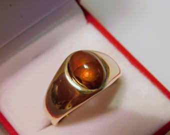 May include: A gold ring with a large, oval-shaped, reddish-brown gemstone set in a bezel setting.