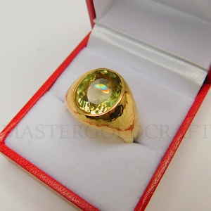 Puede incluir: Un anillo de oro con una gran piedra preciosa verde de forma ovalada. El anillo est&aacute; engastado en una banda de oro martillada.