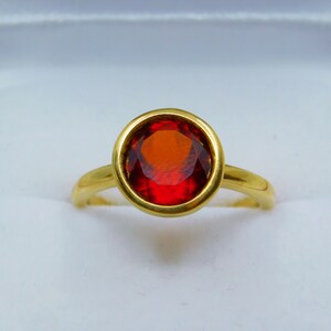 Puede incluir: Un anillo de oro con una piedra ovalada roja engastada.