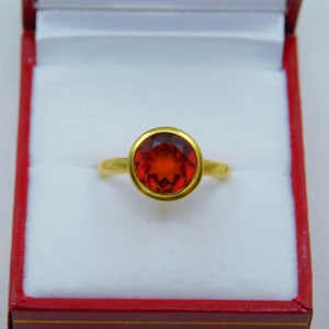 Puede incluir: Un anillo de oro con una gran piedra preciosa roja de forma ovalada engastada en un engaste de bisel.