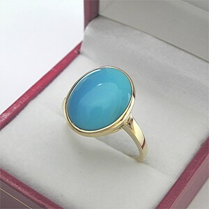 May include: A gold ring with a large oval turquoise gemstone. The ring is in a red velvet ring box.