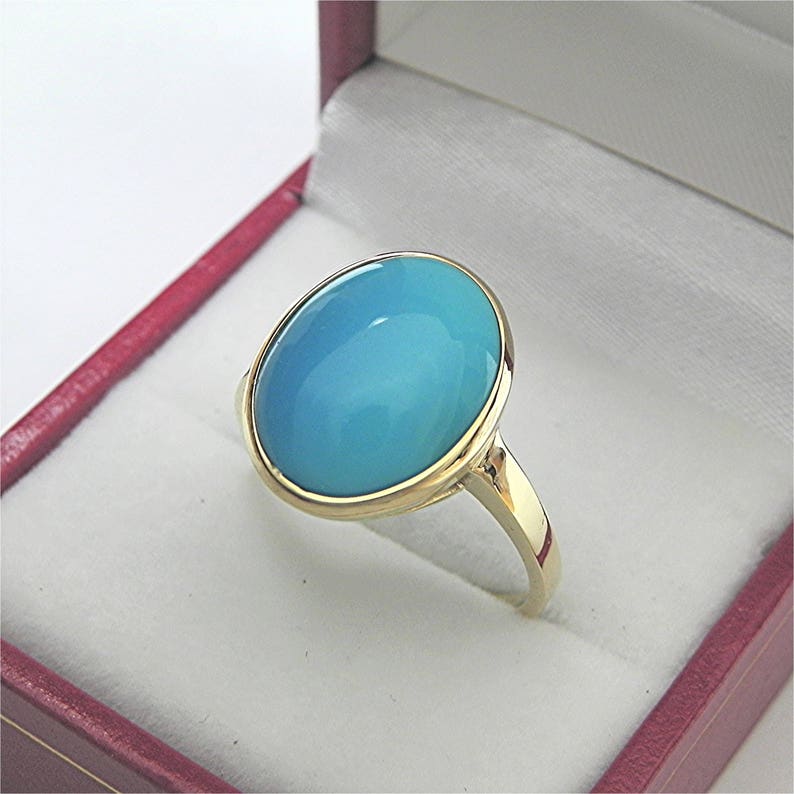 May include: A gold ring with a large oval turquoise gemstone. The ring is in a red velvet ring box.