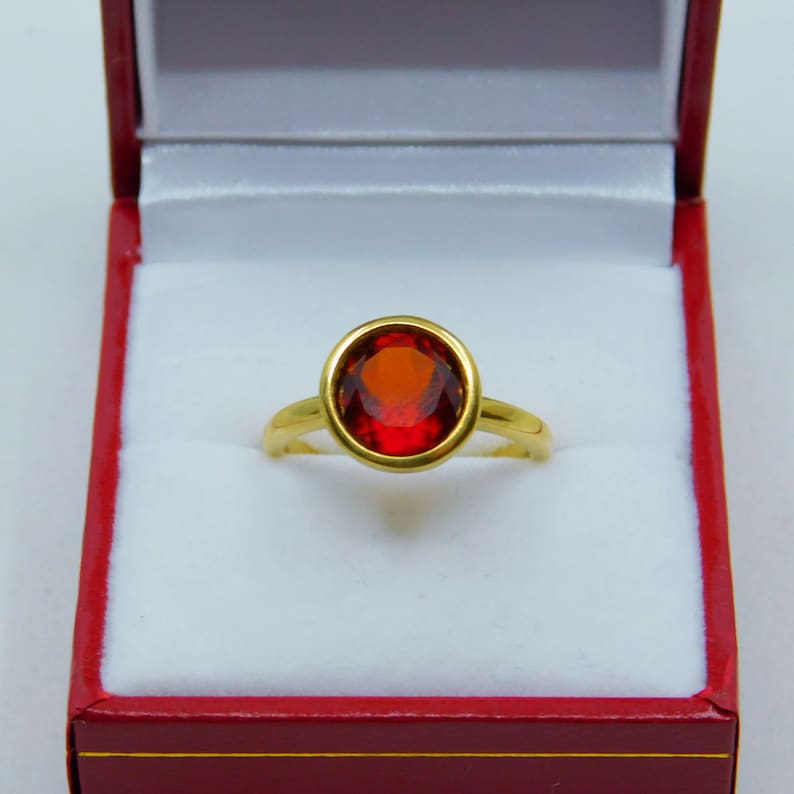Puede incluir: Un anillo de oro con una piedra ovalada roja engastada en un engaste de bisel.