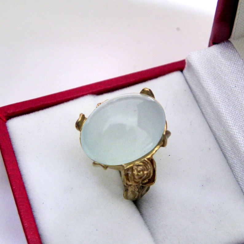 Puede incluir: Un anillo de oro con una gran piedra preciosa ovalada de color blanco lechoso engastada en un dise&ntilde;o de rosa.