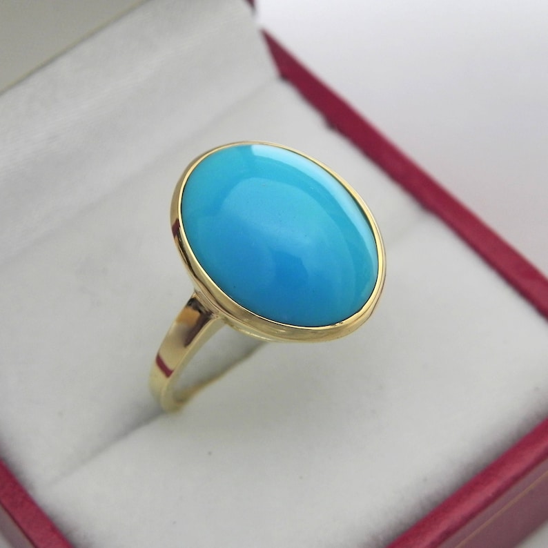 May include: A gold ring with a large oval turquoise gemstone. The ring is set in a gold band and the stone is a bright blue color.