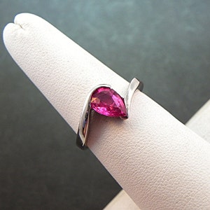 May include: A silver ring with a pear-shaped pink gemstone set in a curved band.