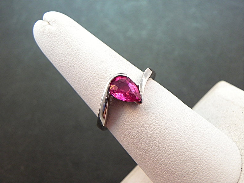May include: A silver ring with a pear-shaped pink gemstone set in a curved band.