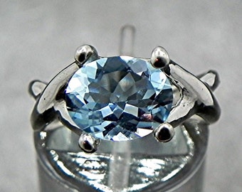 May include: A silver ring with a light blue oval gemstone set in a delicate, twisted band.