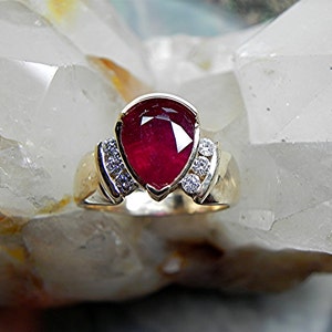 May include: A gold ring with a large, pear-shaped ruby gemstone surrounded by smaller diamonds.