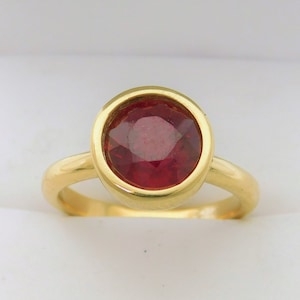 May include: A gold ring with a bezel setting featuring a red gemstone.