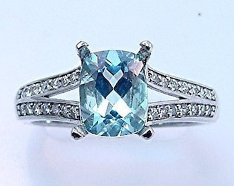 May include: A silver ring with a cushion-cut aquamarine gemstone surrounded by a halo of smaller diamonds. The ring has a split shank with diamonds set along the band.