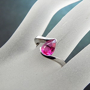 May include: A silver ring with a pear-shaped pink gemstone set in a twisted band.