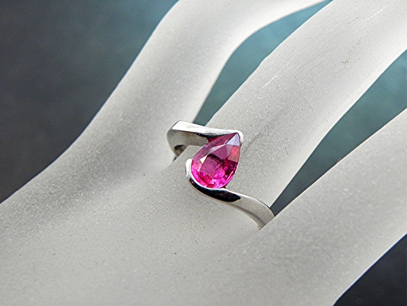 May include: A silver ring with a pear-shaped pink gemstone set in a twisted band.