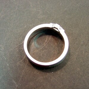 May include: A silver ring with a small, clear stone set in the band.