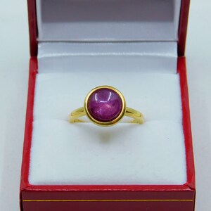 May include: A gold ring featuring a large, round, cabochon-cut, purple gemstone set in a bezel setting.