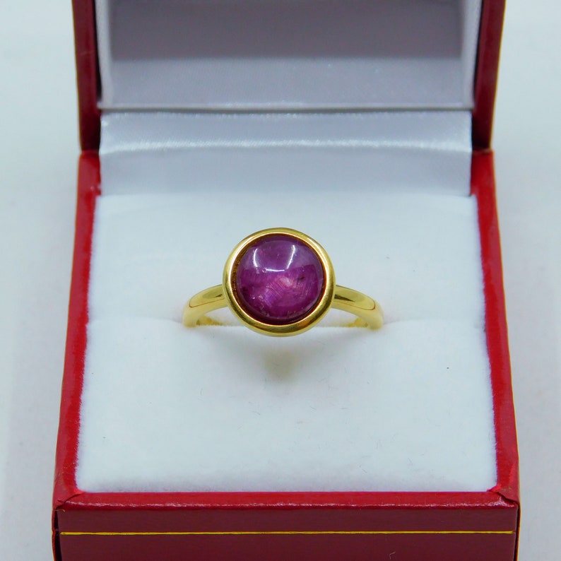 May include: A gold ring featuring a large, round, cabochon-cut, purple gemstone set in a bezel setting.