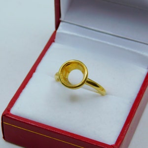 May include: A gold ring with a round bezel setting. The ring is in a red box with white lining.