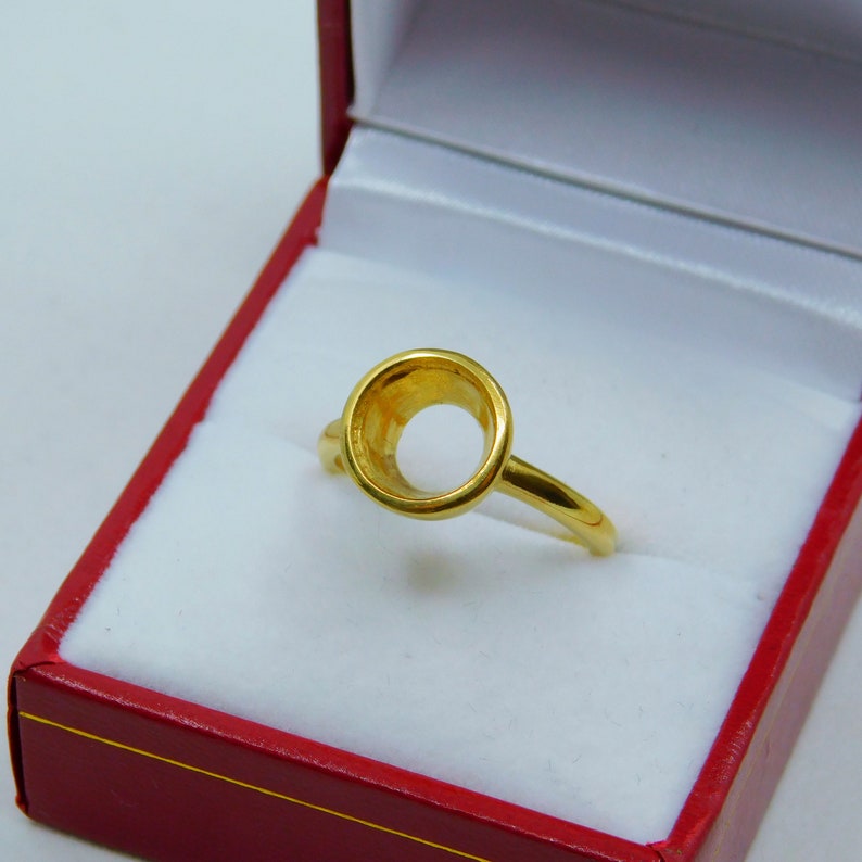 May include: A gold ring with a round bezel setting. The ring is in a red box with white lining.