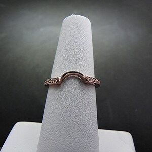 May include: A rose gold ring with a curved design and small clear stones set in the band.