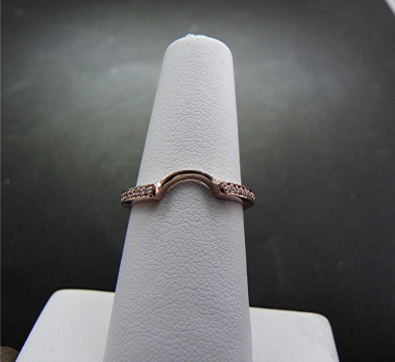 May include: A rose gold ring with a curved design and small clear stones set in the band.