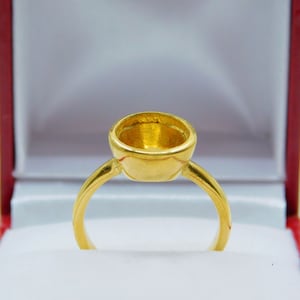 May include: A gold ring with a round, hollow setting. The ring is in a white box.