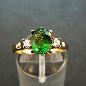 May include: A gold ring with a large oval green gemstone and two smaller round white gemstones.