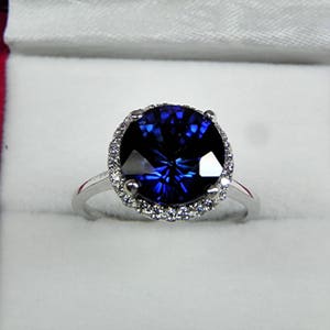 Puede incluir: Un anillo de plata con un gran zafiro azul oscuro redondo rodeado por un halo de diamantes más pequeños.