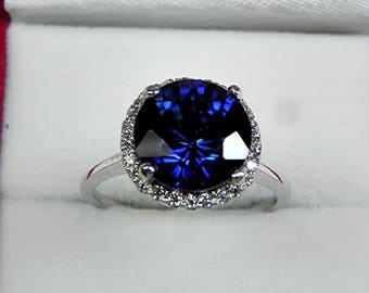 May include: A silver ring featuring a large, round, dark blue sapphire encircled by a halo of smaller diamonds.