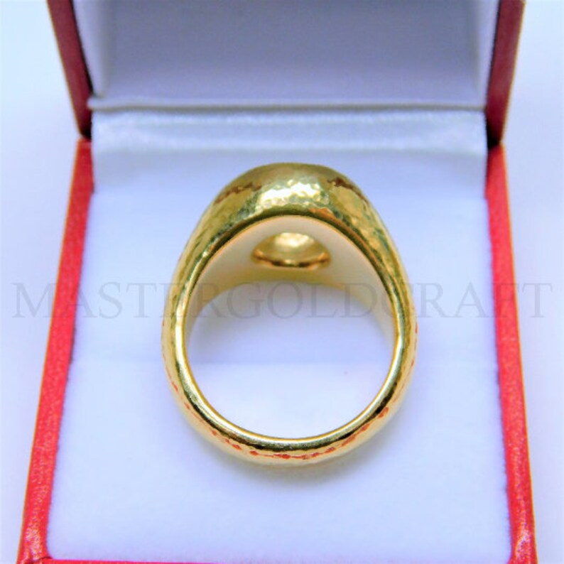 Puede incluir: Un anillo de oro con textura martillada y un centro redondo liso. El anillo se muestra en una caja de terciopelo rojo.