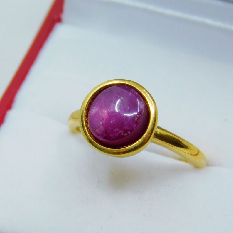 May include: A gold ring featuring a round, cabochon-cut ruby gemstone. The ruby is a deep pink colour and has a star-like pattern.