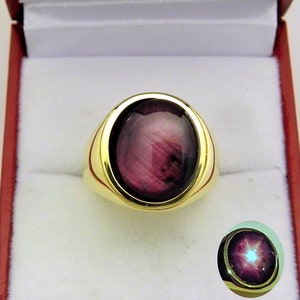May include: A gold ring featuring a large oval-shaped purple gemstone. The gemstone has a star-like pattern in the centre.