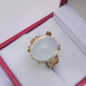 Puede incluir: Un anillo de oro con una gran piedra preciosa ovalada blanca engastada en un dise&ntilde;o floral.